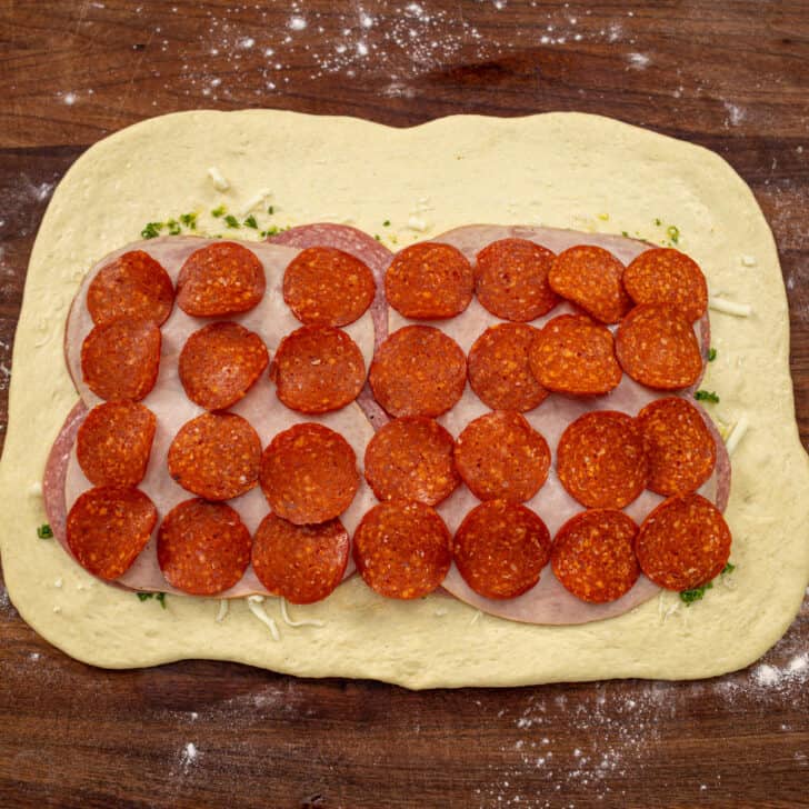 Homemade pizza dough rolled into a rectangle and topped with pepperoni, cheese, salami, and ham for delicious Stromboli