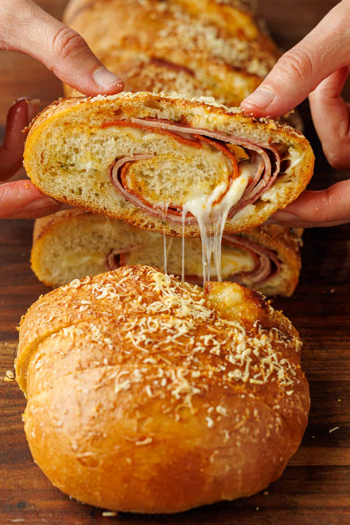 Stromboli sliced into pinwheels showing ham, pepperoni, salami, and melted mozzarella cheese pulls