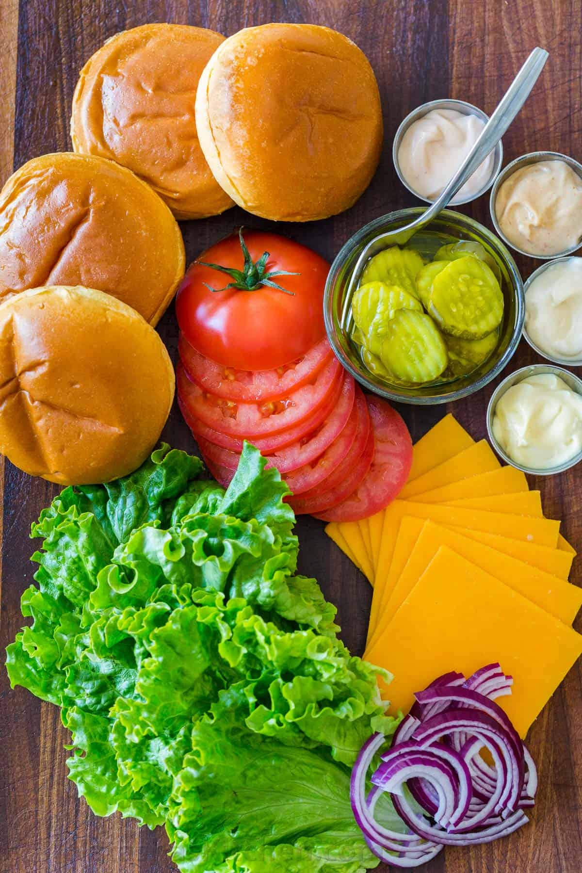 Classic burger toppings with buns, tomatoes, lettuce, cheese, pickles, red onion and sauces