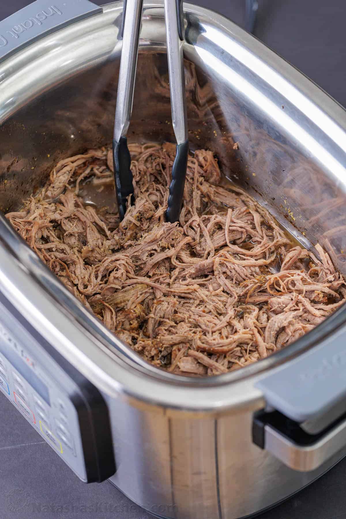 Tongs in a slow cooker with shredded beef 