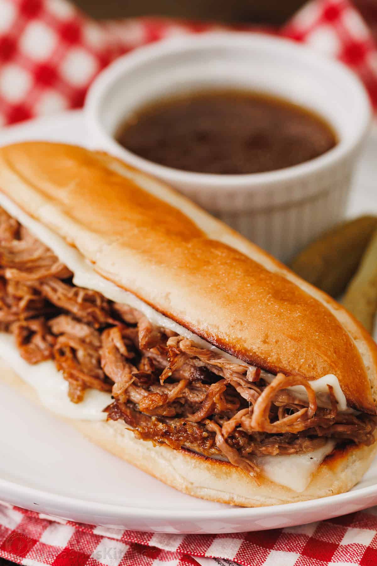 A shredded beef sandwich in a hoagie roll served on white plate next to au jus for dipping.