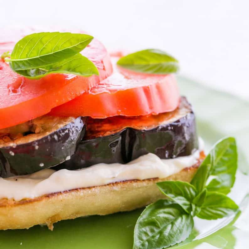 An open-faced eggplant and tomato sandwich garnished with basil on a green plate